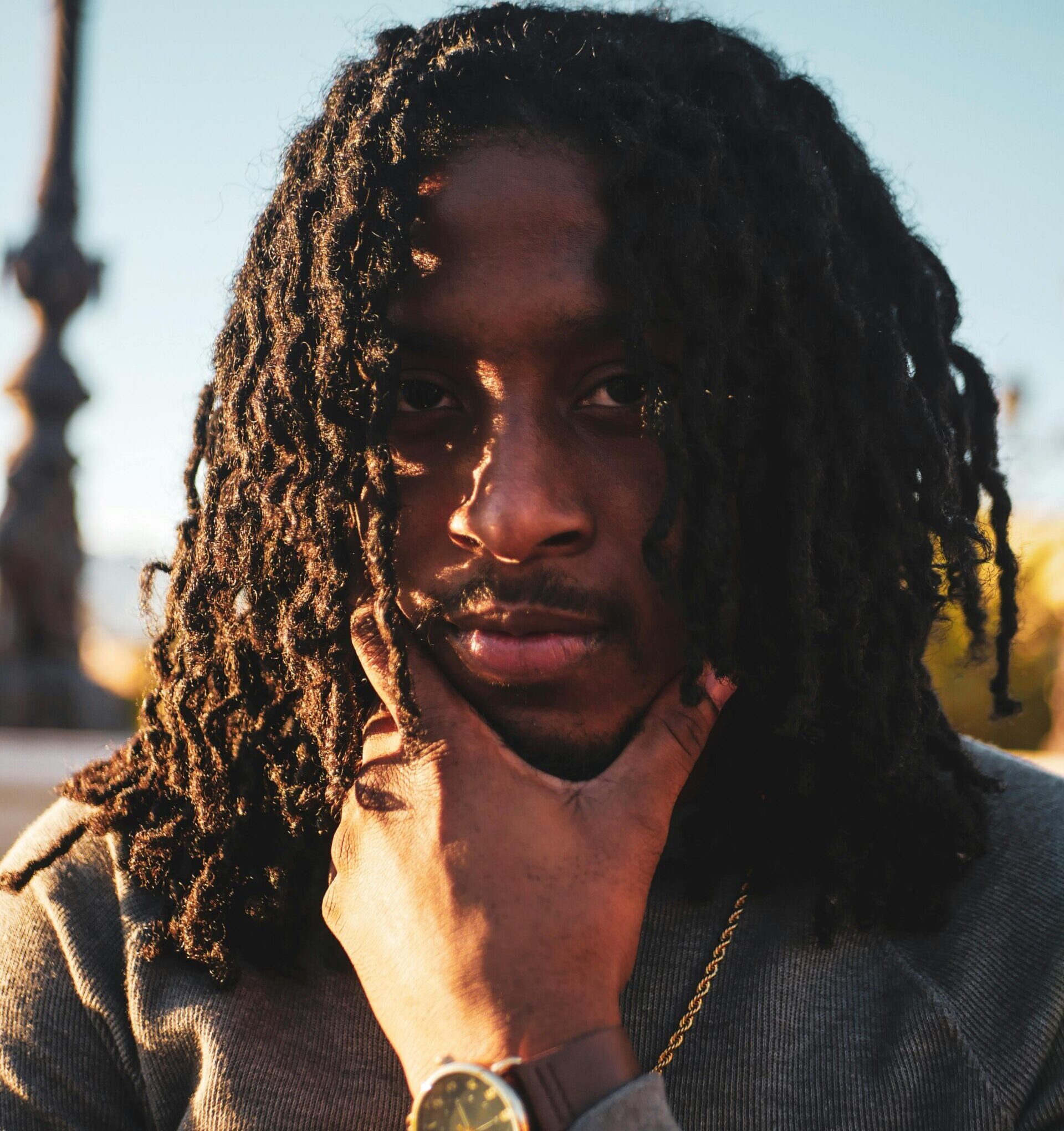A close-up portrait of a man with dreadlocks, thoughtfully posing outdoors in stylish attire.